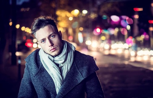 Handsome trendy young man, standing on a sidewalk in city setting at night wearing a fashionable
