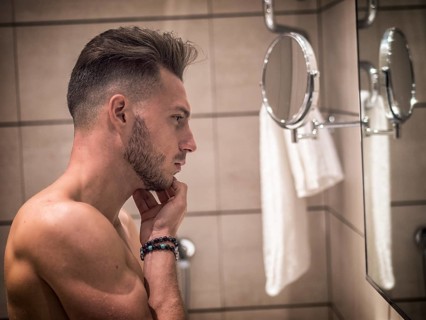 Shirtless muscular handsome young man looking at himself in bathroom mirror in the morning