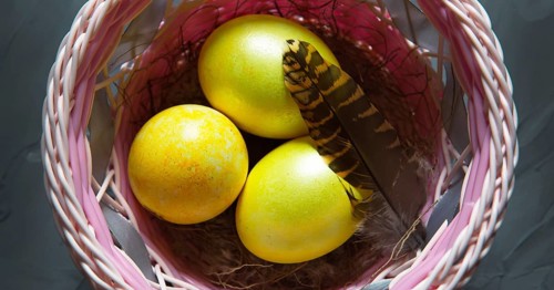 Colorful painted marble shiny Easter eggs in a basket with delicate feathers close-up. Nest with