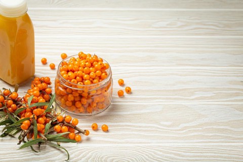 Sea buckthorn healthy drink in bottle, ripe berries in glass jar and branches with leaves top view
