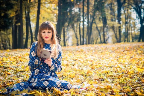 Beautiful girl with long straight hair in a blue long dress reading a book in the autumn park