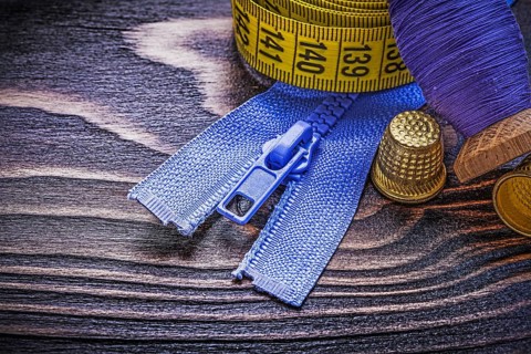 Vintage spool of thread measuring tape thimbles zip fastener on wooden board needlework concept