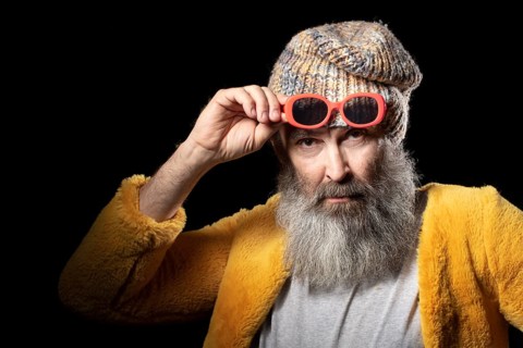 An elderly man with a grey beard wearing a knitted hat and a bright yellow fur coat. Fashionable