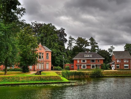 Houses on the lakeshore, surrounded by trees and plants, with a cloudy sky, groenlo, gelderland,