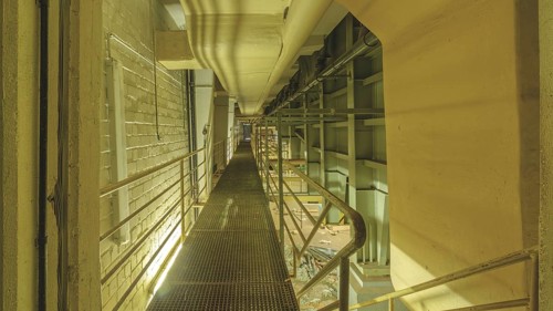 Industrial interior with a raised walkway and metal grating, surrounded by pipes and railings, Bad