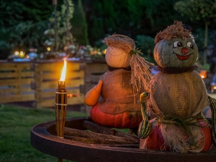 Two pumpkin sculptures sitting on a wooden wheel, illuminated by a burning torch in the evening