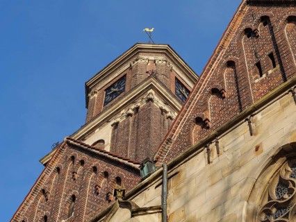 A pointed brick church tower with decorative details and clock under a bright blue sky, Coesfeld,