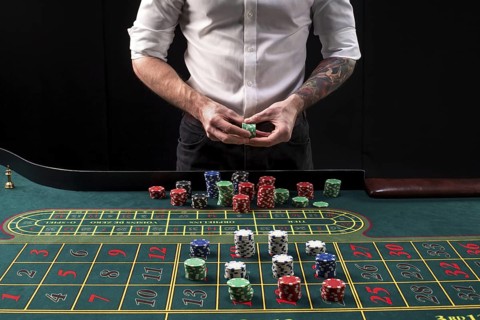A close-up vibrant image of green casino table with roulette, with the hands of croupier and