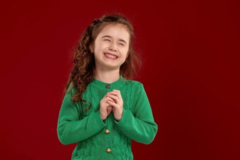 Portrait of a laughing tiny kid with a long, curly hair looking happy. Charming girl in a knitted