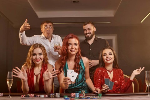 Happy friends are playing poker at casino. They are celebrating their win, smiling and posing at