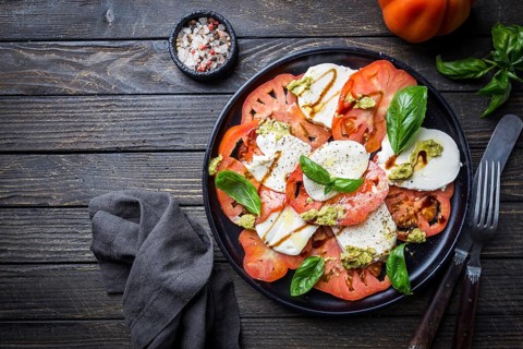 Italian caprese salad with sliced tomatoes, mozzarella cheese, basil, olive oil. Served on black