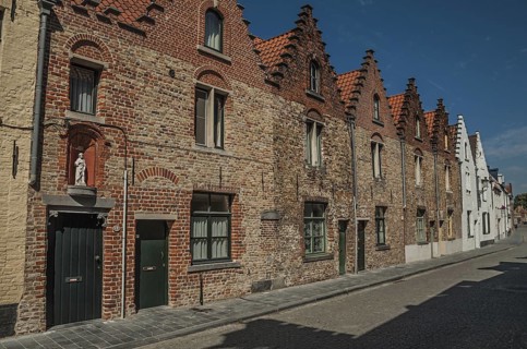 Brick facade of old houses with a blue sunny sky in an empty street of Bruges. With many canals and