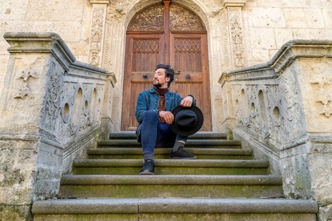 Portrait of a young man sitting against a beautiful old medieval cathedral door. A man in front of