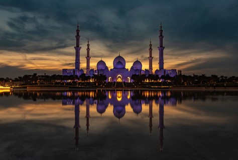 A picture of the Sheikh Zayed Grand Mosque reflected on the Oasis of Dignity pool, at sunset