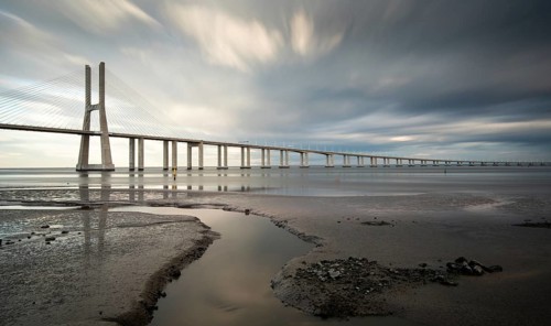 Vasco da Gama Bridge at sunset with dramatic cloudy sky in Lisbon Portugal. Long exposure