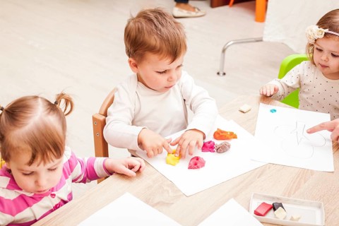 The teacher helps the girl to make a figure plasticine on the table