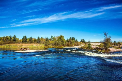 Thin flying cirrus clouds and broad Winnipeg River. Landscape in the Old Pinawa Dam Park. Trend of