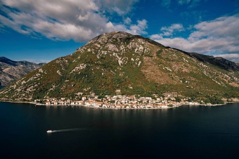 Boat sails along the Bay of Kotor against the backdrop of the coast of Perast at the foot of the