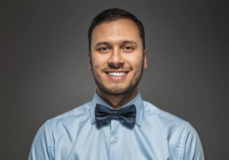 Portrait of happy smiling young man in blue shirt and butterfly tie isolated over gray studio