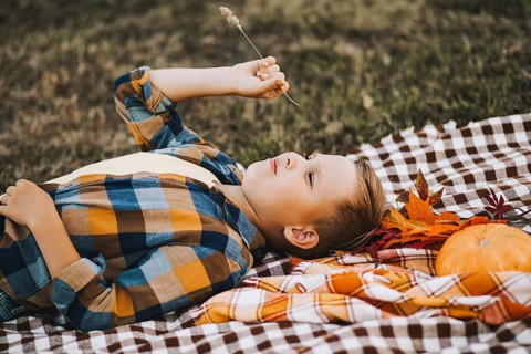 Kid boy lies near a river, pond or lake and smiling. Autumn season. Happy childhood