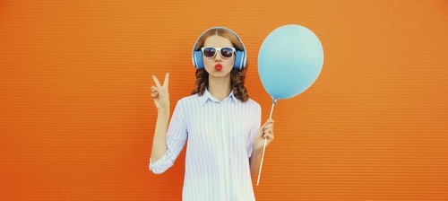Portrait of happy cheerful young woman in wireless headphones listening to music with balloon on