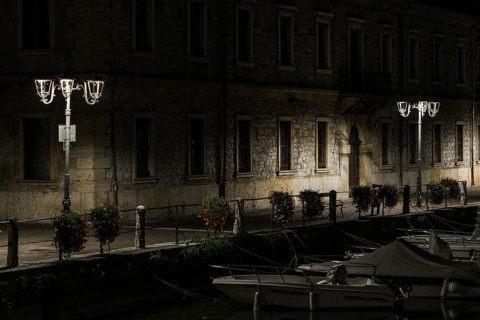 A canal view at night with moored boats, a stone building, and lampposts creating tranquil shadows,