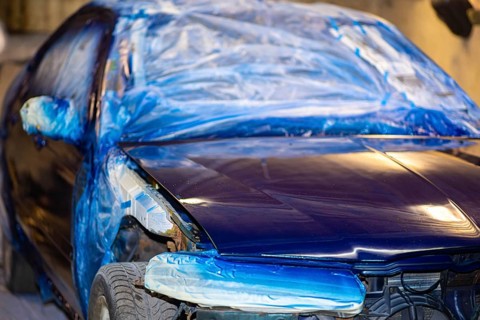 A blue car partially covered with plastic sheeting in a workshop setting