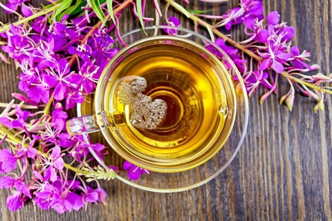 Herbal tea in a glass cup, fresh flowers fireweed against the backdrop of wooden planks on top