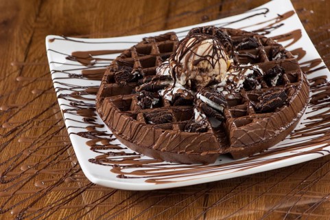 Wafer cake in a square white plate on a wooden lacquered surface with reflection