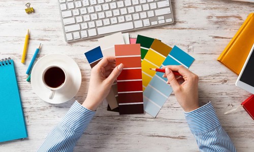 Web designer choosing colors from swatches at wooden desk. Office workplace with computer keyboard