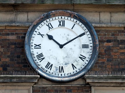 Old round clock on the brick wall of a building with roman numerals with hands at ten past ten
