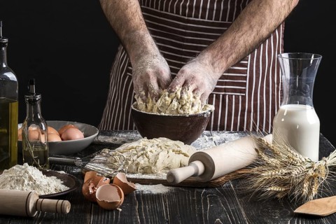 A handful of flour with egg on a rustic kitchen. Against the background of men's hands knead the