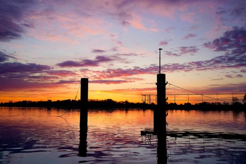 Bollard on the water in a pink morning sky with atmospheric reflection at dusk, An der Kaje /