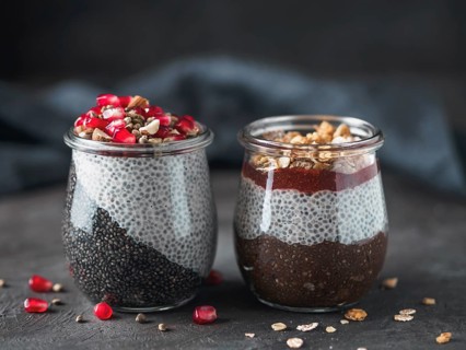 Two chia pudding in glass jars on dark table. Two colors charcoal chia puding with pomegranate,