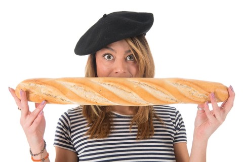 Young French girl with typical French barret and striped shirt eating bread isolated over white
