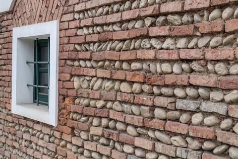 Oblique view of a wall made of bricks and river stones with a green window
