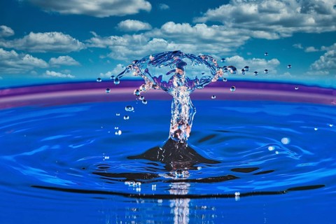 A splashing drop of water in front of a blue sky with white clouds, highspeed photography, drop