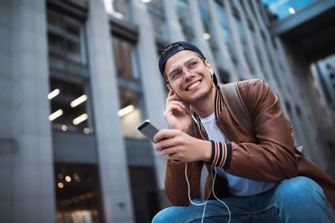 Man Sitting Listening Music Earphones Concept. Cheerful young guy listening the music
