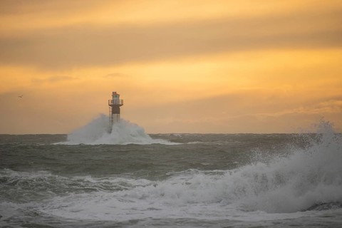 A lighthouse stands in the storm. Wild sea in the evening. Sunset on a coast with many rocks in the