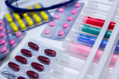 Various colorful pills and test tubes arranged on a lab table with glasses