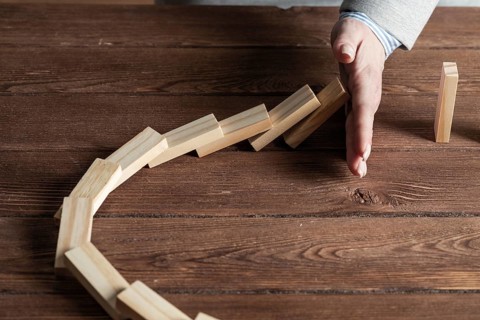 Businesswoman protecting dominoes from falling on wooden desk. Business assistance and leadership