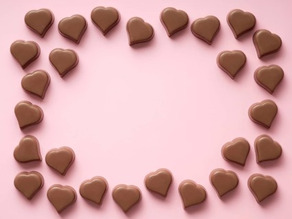 Frame of romantic chocolate confections in heart shapes on pastel pink background. Canvas with