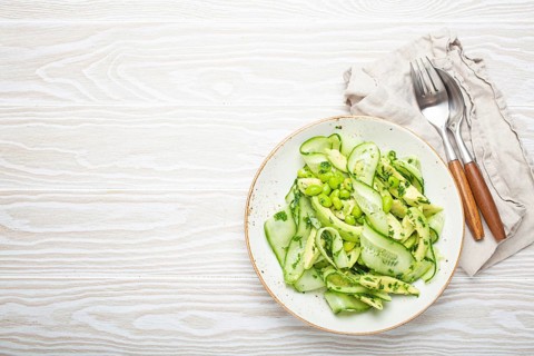 Healthy vegan green avocado salad bowl with sliced cucumbers, edamame beans, olive oil and herbs on