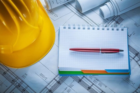 Hard hat checked notebook pen blueprints on construction drawing