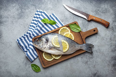 Raw fish dorado in casserole dish with ingredients lemon, fresh basil, bottle of olive oil on