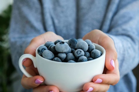 Woman holding bowl with Frozen blueberry fruits. Harvesting concept. Female hands collecting