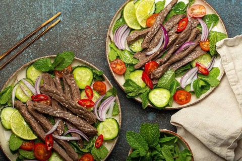 Two plates with traditional Thai beef salad with vegetables and mint top view served on rustic