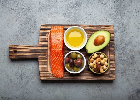 Food sources of healthy unsaturated fat: fresh raw salmon fillet, avocado, olives, nuts on cutting