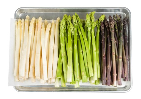 White, green and purple asparagus on a baking tray on a white background
