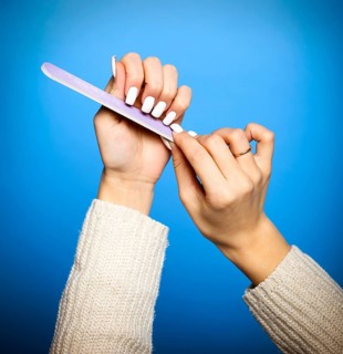 Faceless female in sweater filing long white nails doing manicure on blue background